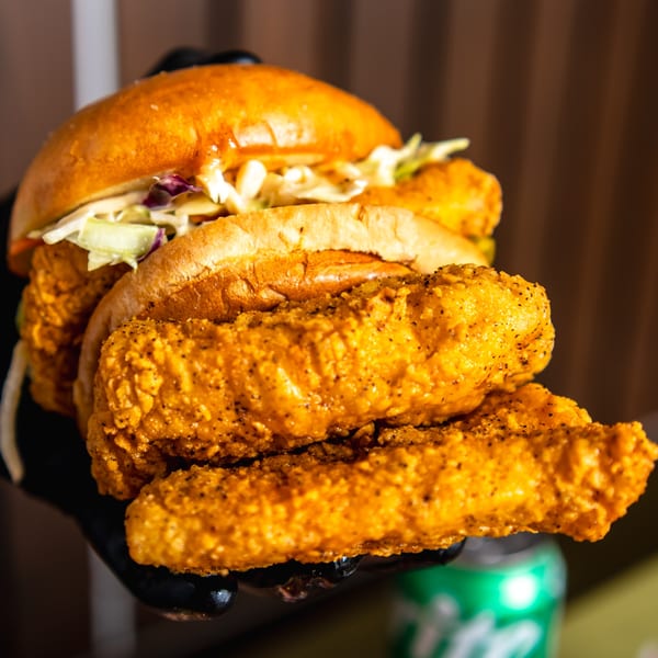 A Bird Haus fried chicken sandwich with coleslaw and two chicken tenders held by a gloved hand.