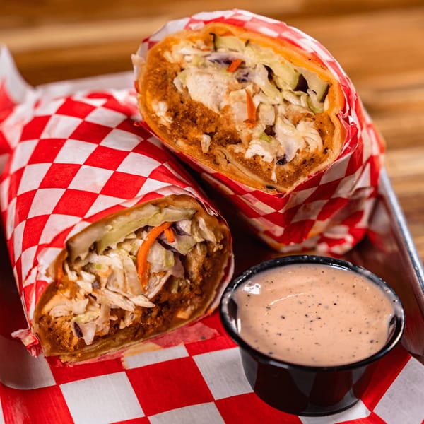 Two Bird Haus fried chicken wraps with coleslaw, served with a side of dipping sauce.
