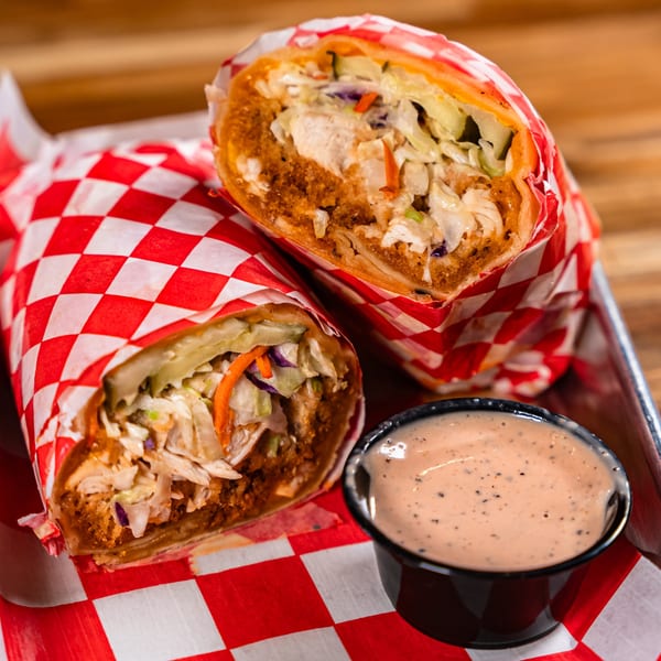 Two Bird Haus fried chicken wraps with coleslaw, served with a side of dipping sauce.